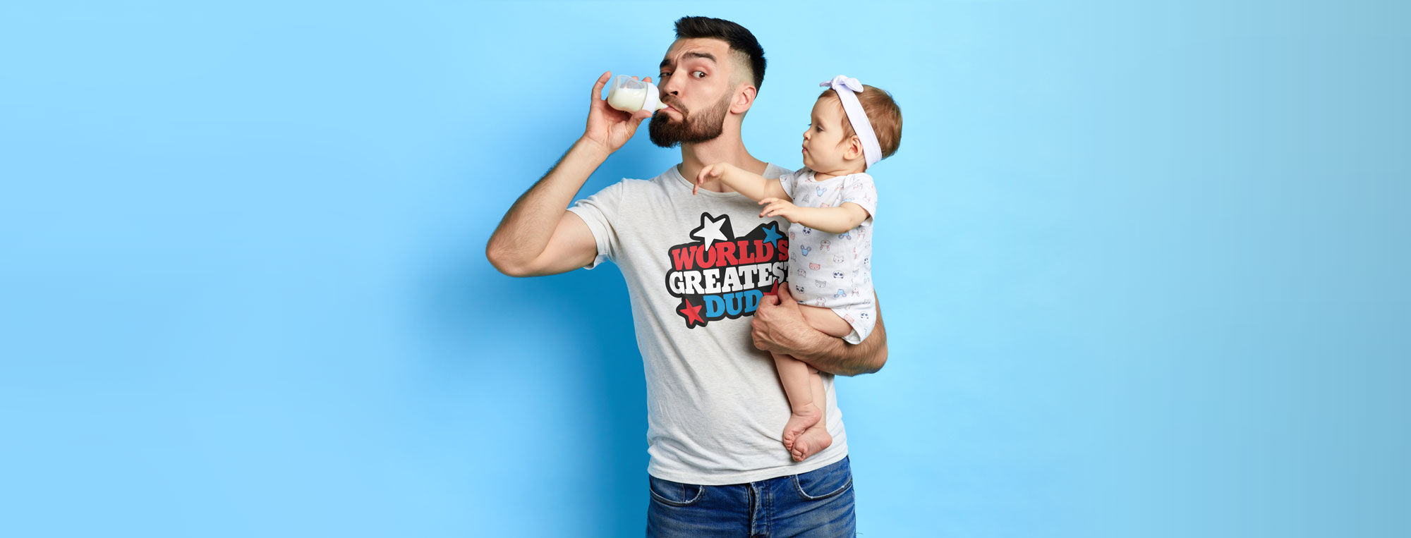 First-time dad sneaking milk from a baby bottle wearing funny dad t-shirt from World's Greatest Dud brand.